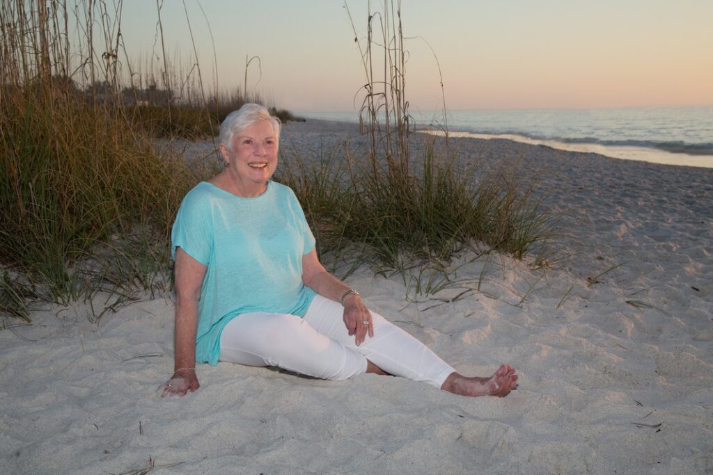 business portrait of a woman on the beach seated in the sand wearing a blue blouse and white pants