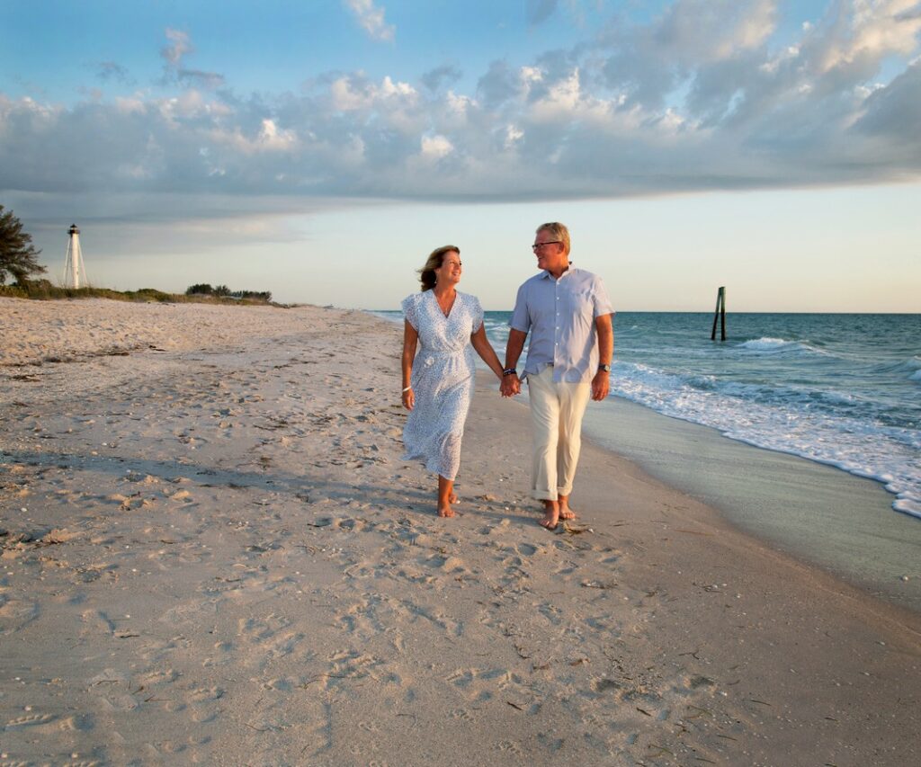 portrait of a couple holding hands and walking along the beach near the Range Light in Boca Grande, FL