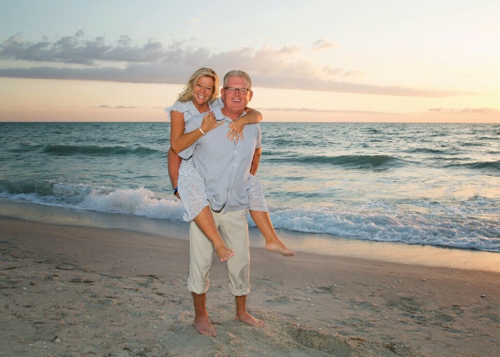 middle aged man giving his wife a piggyback ride on the beach at sunset