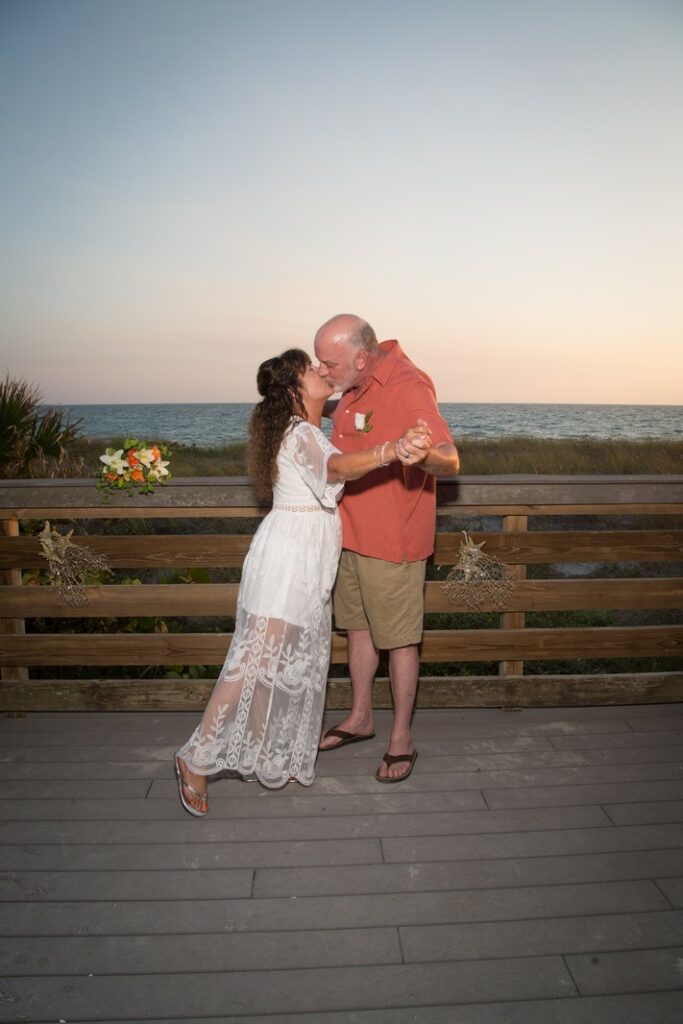 mature bride and groom kissing while standing on a boardwalk at the beach
