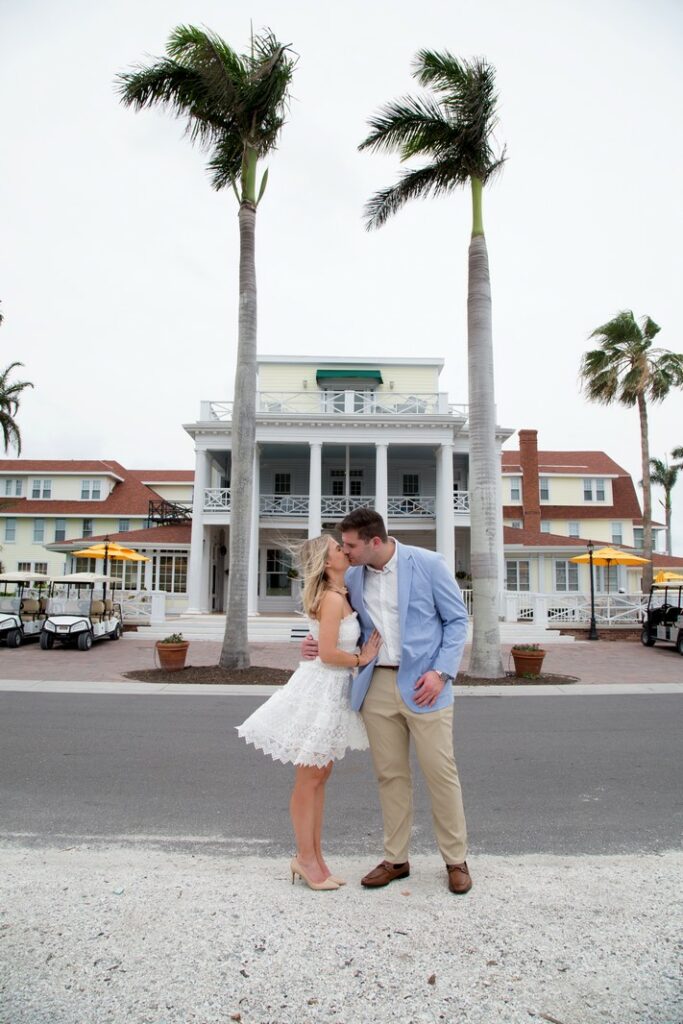 wedding photo of a bride in a short dress and a groom in a light blue sport coast kissing in front of the Gasparilla Inn